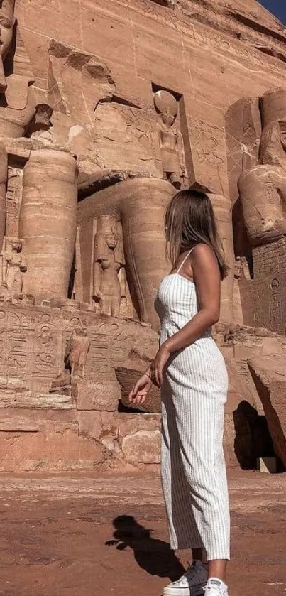 A woman stands in front of ancient Egyptian carvings under a clear blue sky.