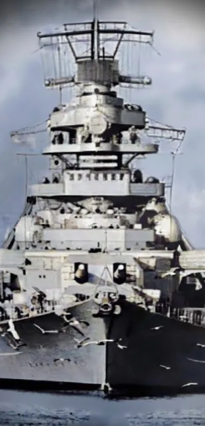 Front view of a majestic battleship on calm waters under a cloudy sky.