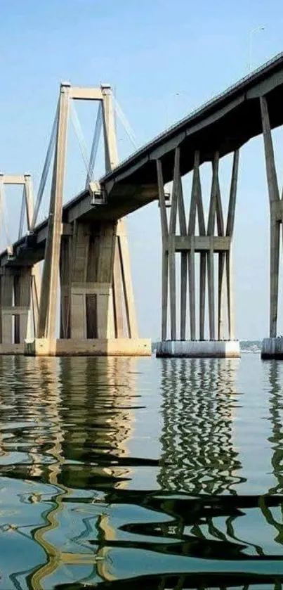 A majestic bridge reflecting in calm water under a clear sky.