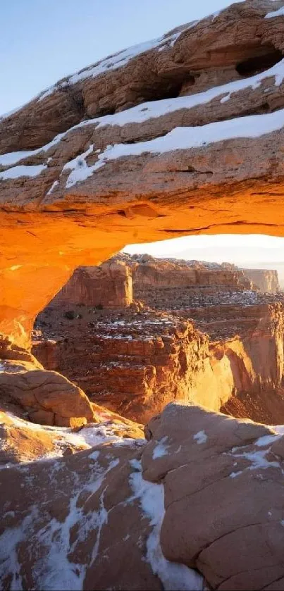 Sunset over snow-capped canyon with natural arch.