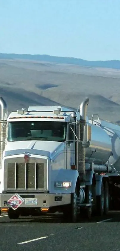 Silver tanker truck on open highway under clear sky.