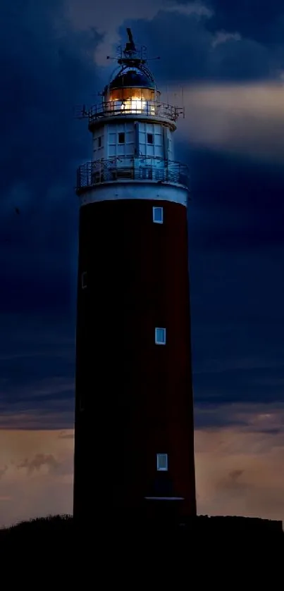 A lighthouse at night with a deep blue sky and a glowing light.