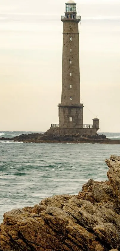 A tall lighthouse stands by the rocky sea shore under a beige sky.