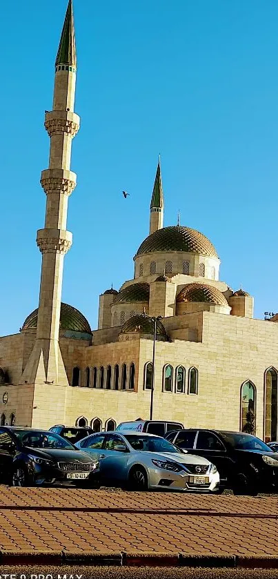 Majestic mosque with blue sky and cars parked in front.