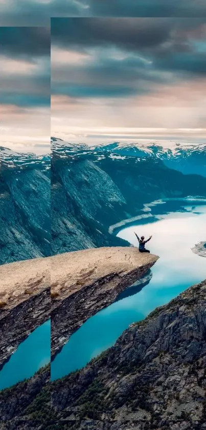 Person on cliff with mountain lake and blue sky.