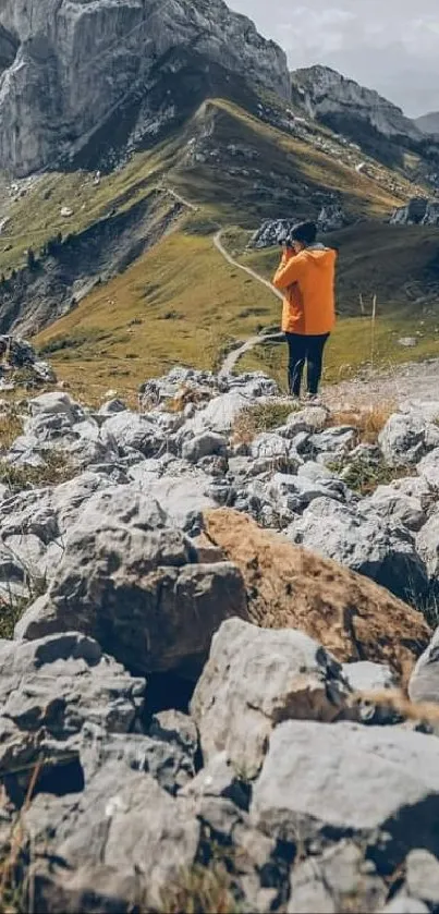 A hiker in orange amidst a stunning mountain landscape with rocky terrain.