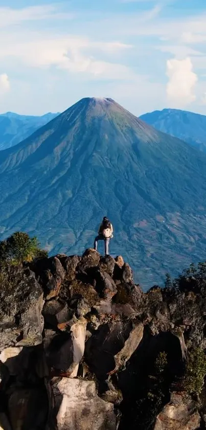 Person standing on rocks with mountain and sky in the background.