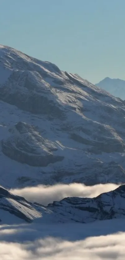 Snow-covered mountains with misty clouds under a blue sky.