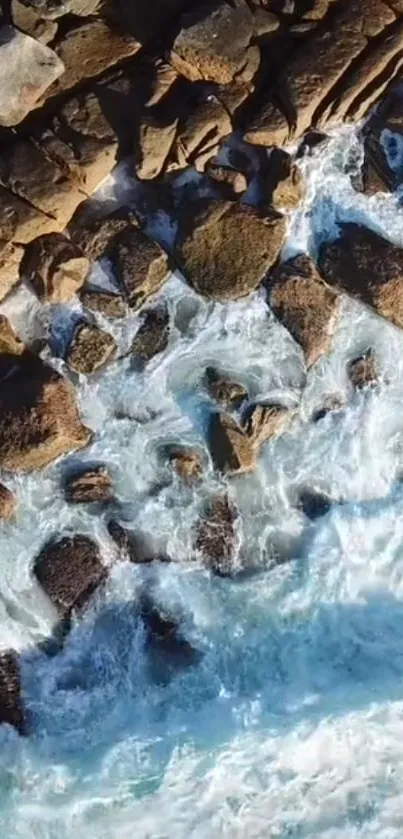 Aerial view of ocean waves crashing against rugged rocks on a sunny day.