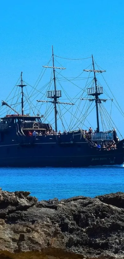 A pirate ship sails across the vibrant blue ocean with a clear sky backdrop.