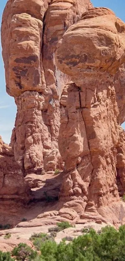 Majestic red rock formation under a clear blue sky with green foliage.