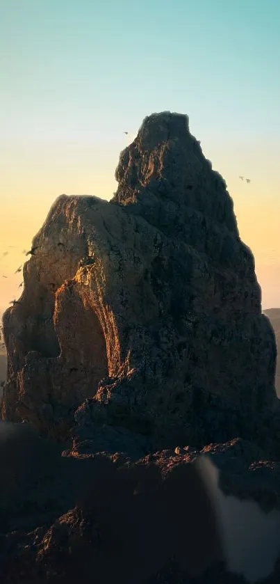 Majestic rocky mountain at sunset with birds flying in a serene orange and blue sky.