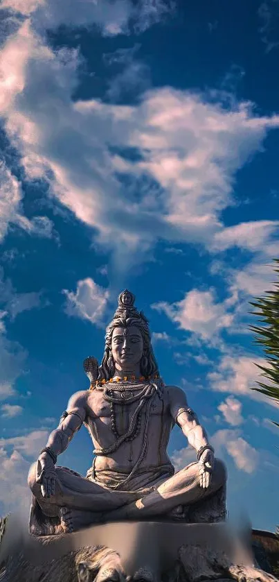 Statue of Shiva against a blue sky with clouds.