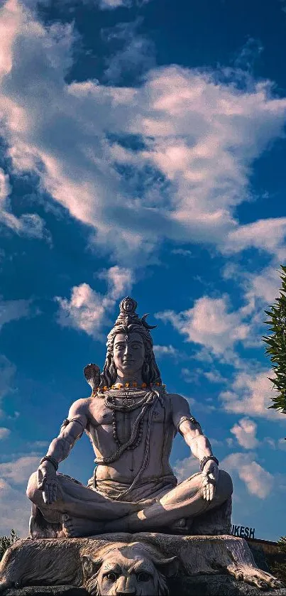 Shiva statue under a vibrant blue sky with clouds and greenery.