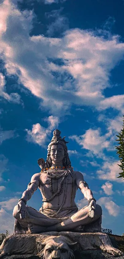 Majestic Shiva statue under a vibrant blue sky with clouds and greenery.