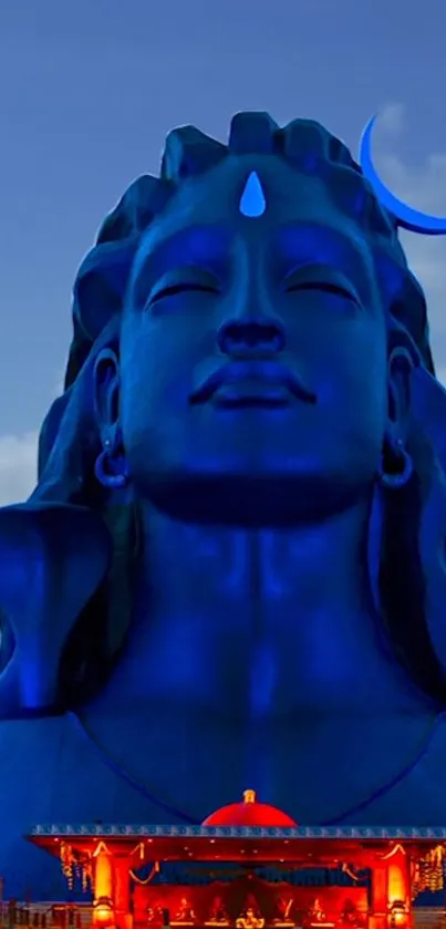 Blue statue of Shiva under a crescent moon with clouds in the background.