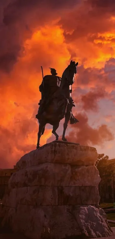 Silhouette of an equestrian statue against a vibrant orange sunset sky.