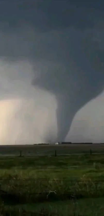 Tornado swirling under a dark sky with open land in view.