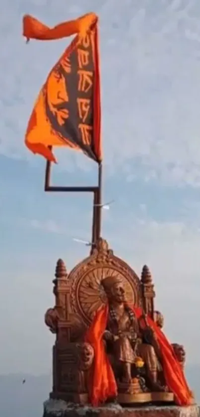 Majestic warrior statue with orange flag against a cloudy sky.