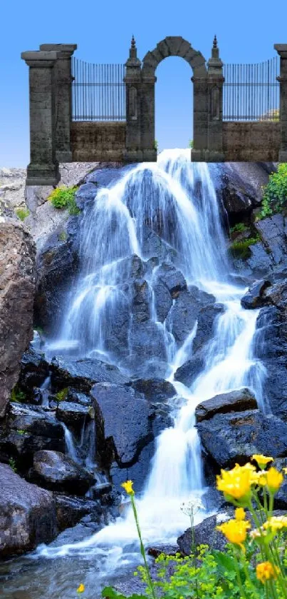 Waterfall beneath stone arch with wildflowers and blue sky.