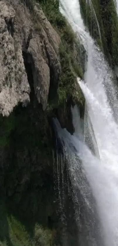 Majestic waterfall cascading over rocky cliff in lush green scenery.