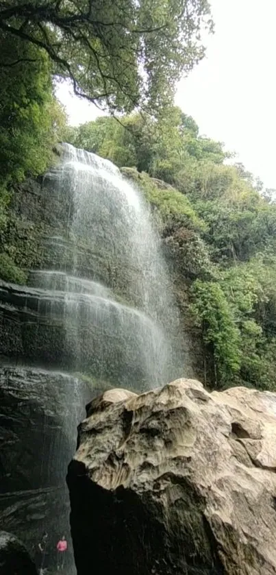 Majestic waterfall cascades in lush forest setting, surrounded by rocky cliffs.