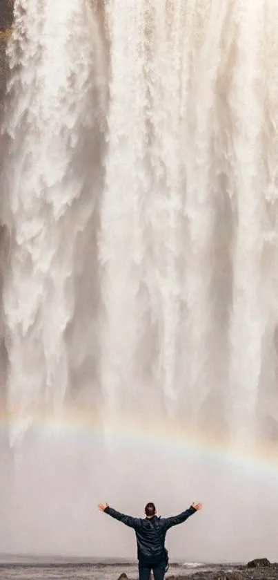 Person in front of a massive waterfall with a rainbow arc at the bottom.