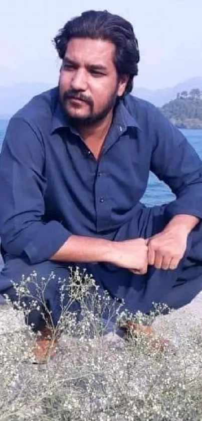 Man in blue sitting by a tranquil lake with serene natural scenery.