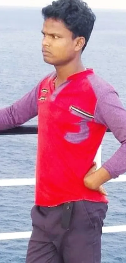 Man in red shirt standing by the ocean on a sunny day.