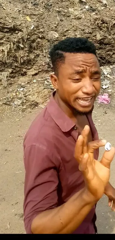 Man in maroon shirt holding a button outdoors.