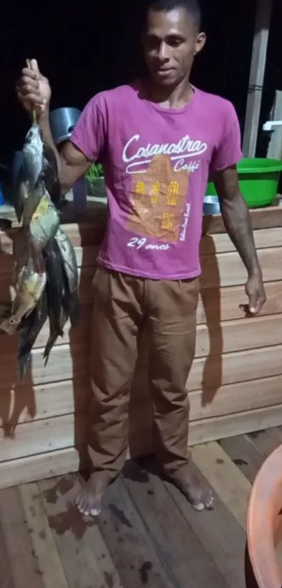 Man standing on wood floor holding fish at night.