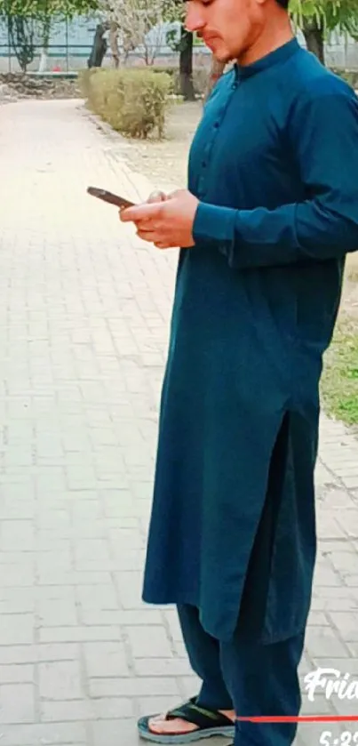 A man in a blue kurta checks his phone outside.