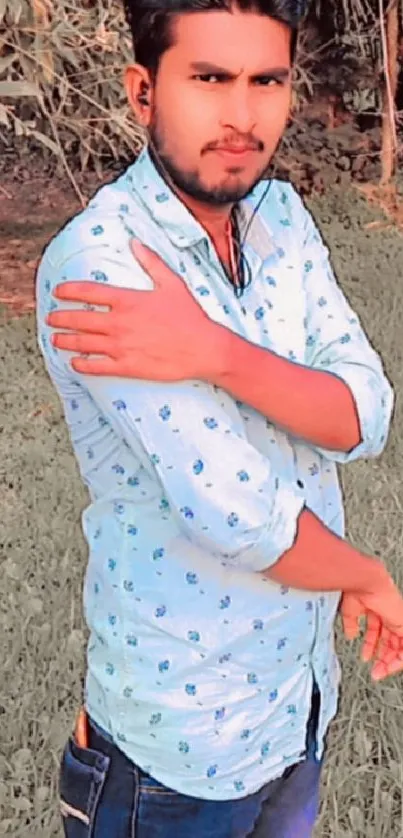 Man in a blue patterned shirt standing outdoors in nature.