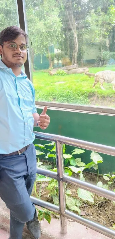 Man in blue shirt poses near white tiger in a lush, green zoo setting.