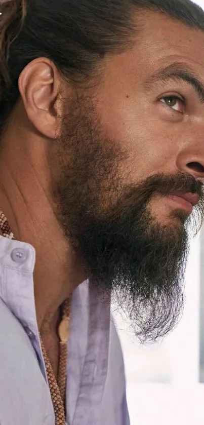 Portrait of a bearded man wearing a lilac shirt with a topknot.