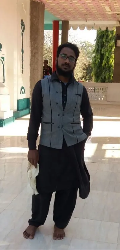 Man in traditional attire standing indoors with soft lighting.