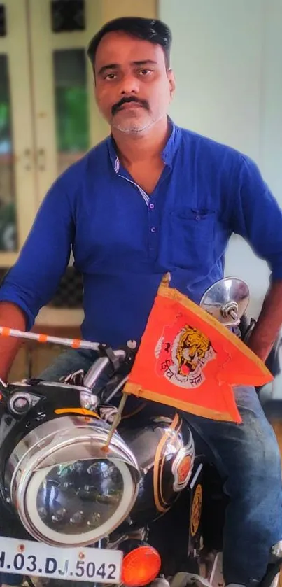 A man in a blue shirt on a motorcycle with an orange flag.