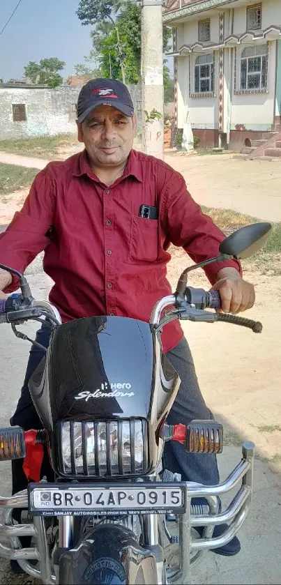 Man wearing red shirt sitting on a motorcycle in a rural setting.