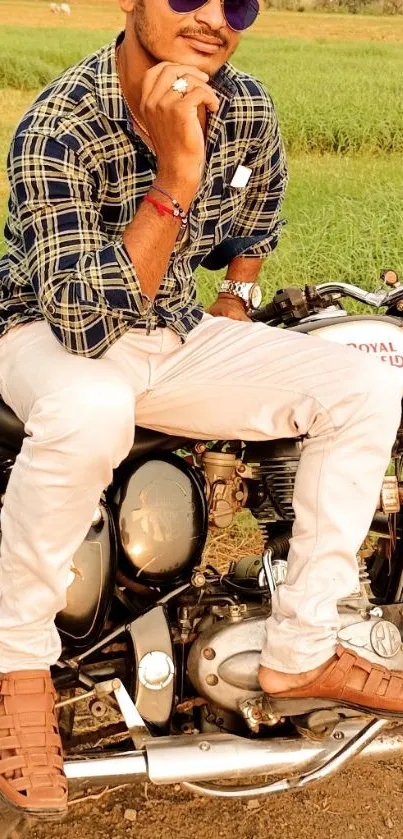 Man sitting on a classic motorcycle with sunglasses against a green field backdrop.