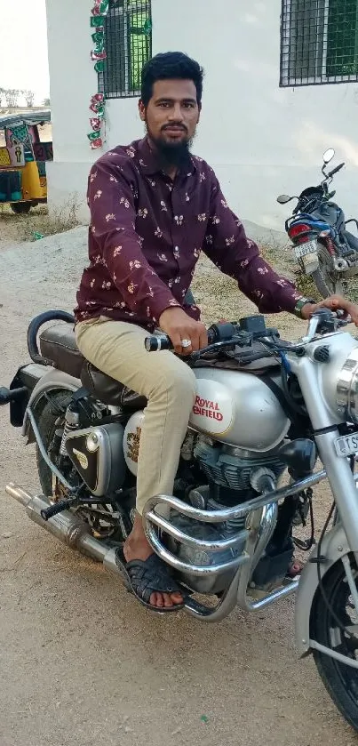 Man on silver Royal Enfield motorcycle, parked outdoors.