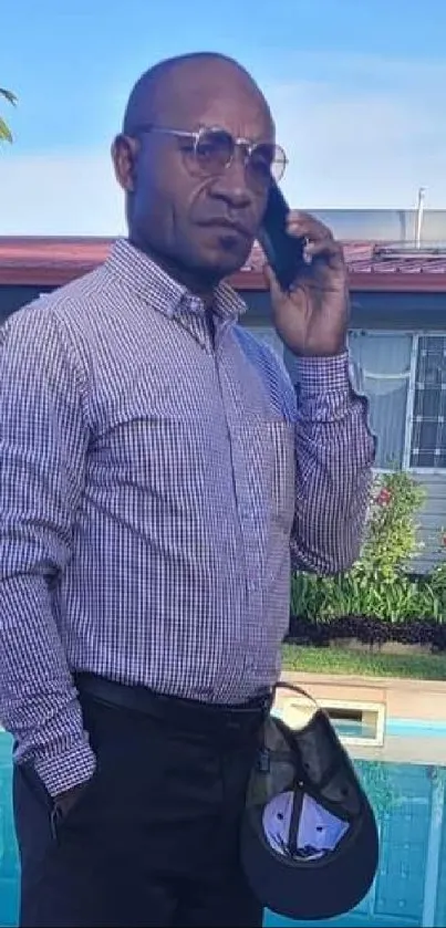 Man in a plaid shirt on phone near a pool.