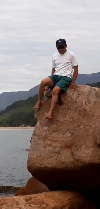 Man sitting on a rocky cliff overlooking the ocean and cloudy sky.