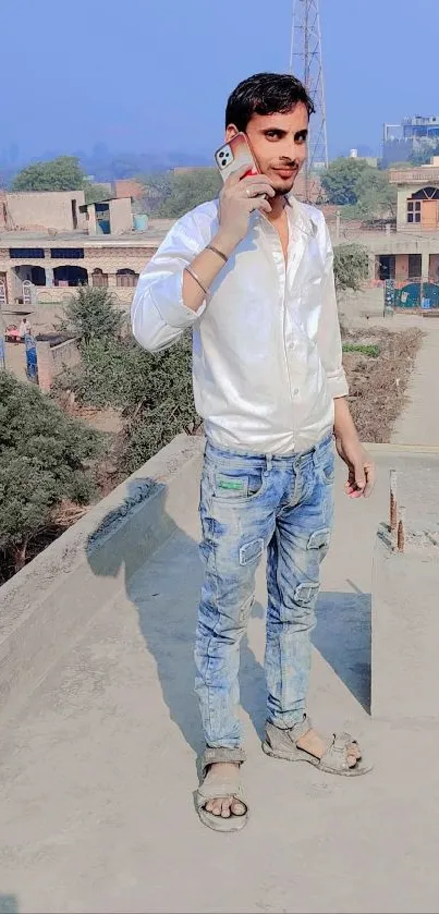 Man in white shirt on rooftop with phone, city view.