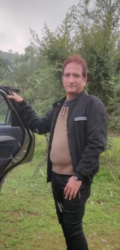 Man standing by a car in a lush green setting.