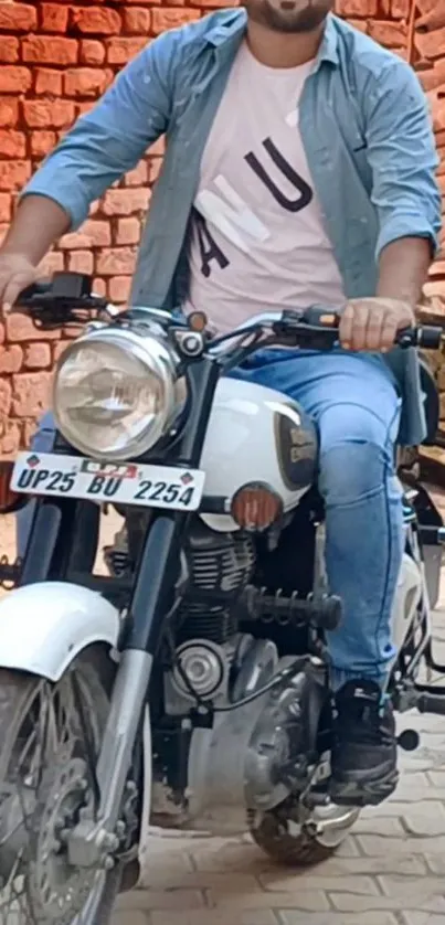 Man riding a classic motorcycle with brick background.