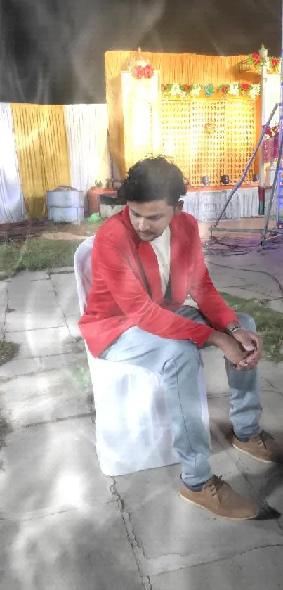 Man in red jacket sitting on stone pavement at night event.