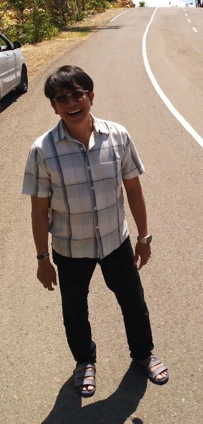 Man smiling on a sunny road, wearing a checkered shirt.