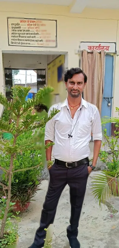 Man standing outdoors with plants and building.