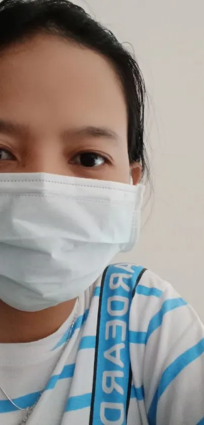 Person wearing a mask with blue striped shirt on a light background.