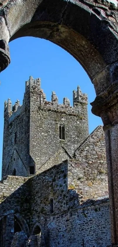 Stone castle framed by ancient arches under a blue sky.